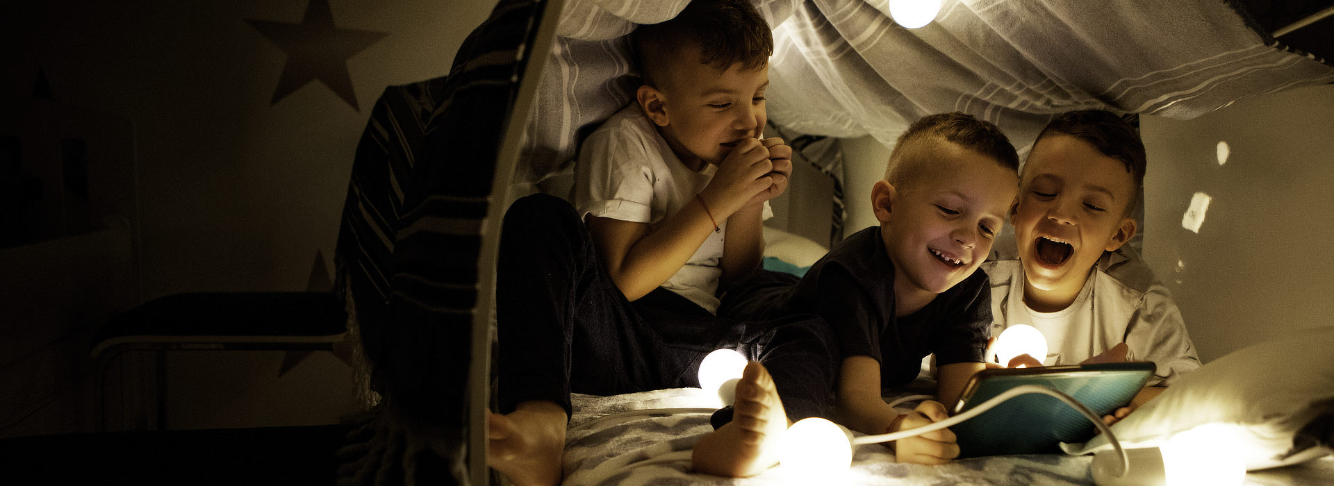 Kinder mit Lichterkette in einer selbstgebauten Kissenburg